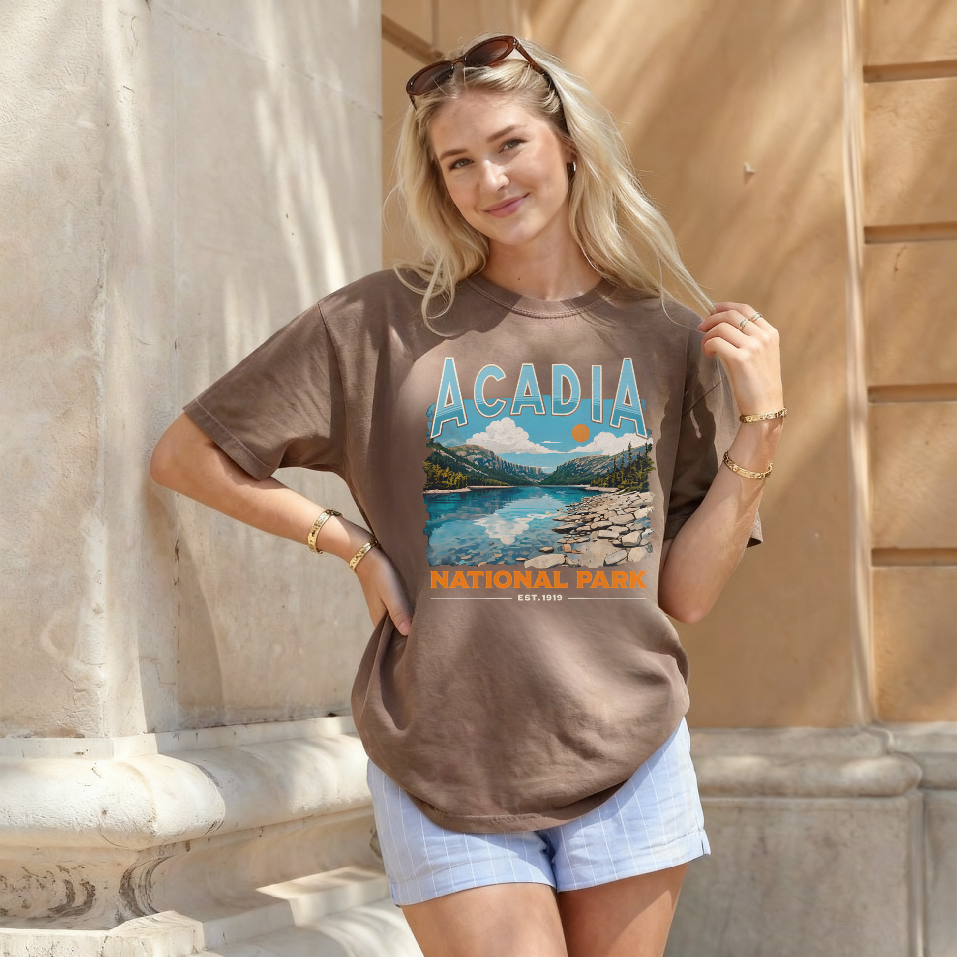 Woman wearing espresso brown Acadia National Park graphic tee with scenic landscape artwork styled with light blue shorts.