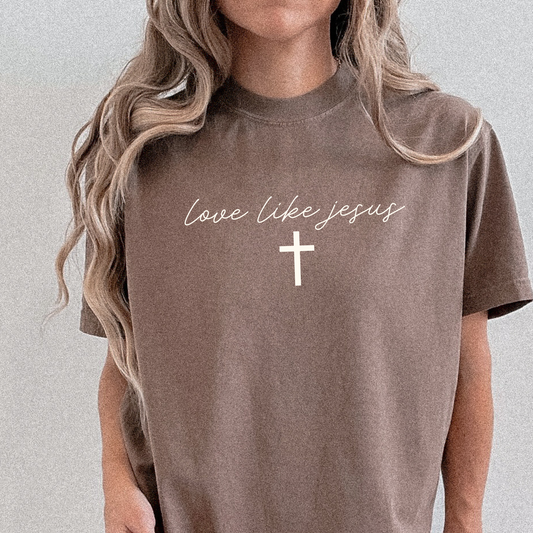 Woman wearing espresso Comfort Colors tee with “Love Like Jesus” script and white cross graphic, Christian faith t-shirt.