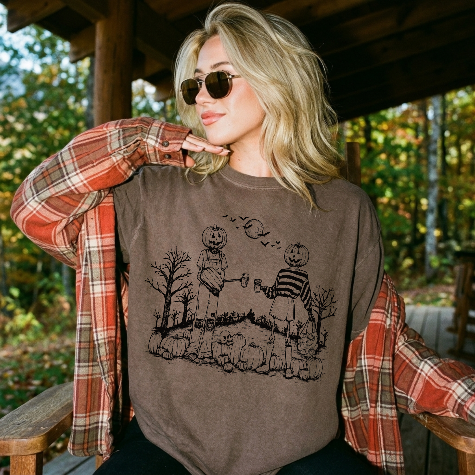 Woman wearing an espresso brown Halloween graphic tee featuring two pumpkin-headed friends holding coffee surrounded by pumpkins under a spooky moon during autumn.