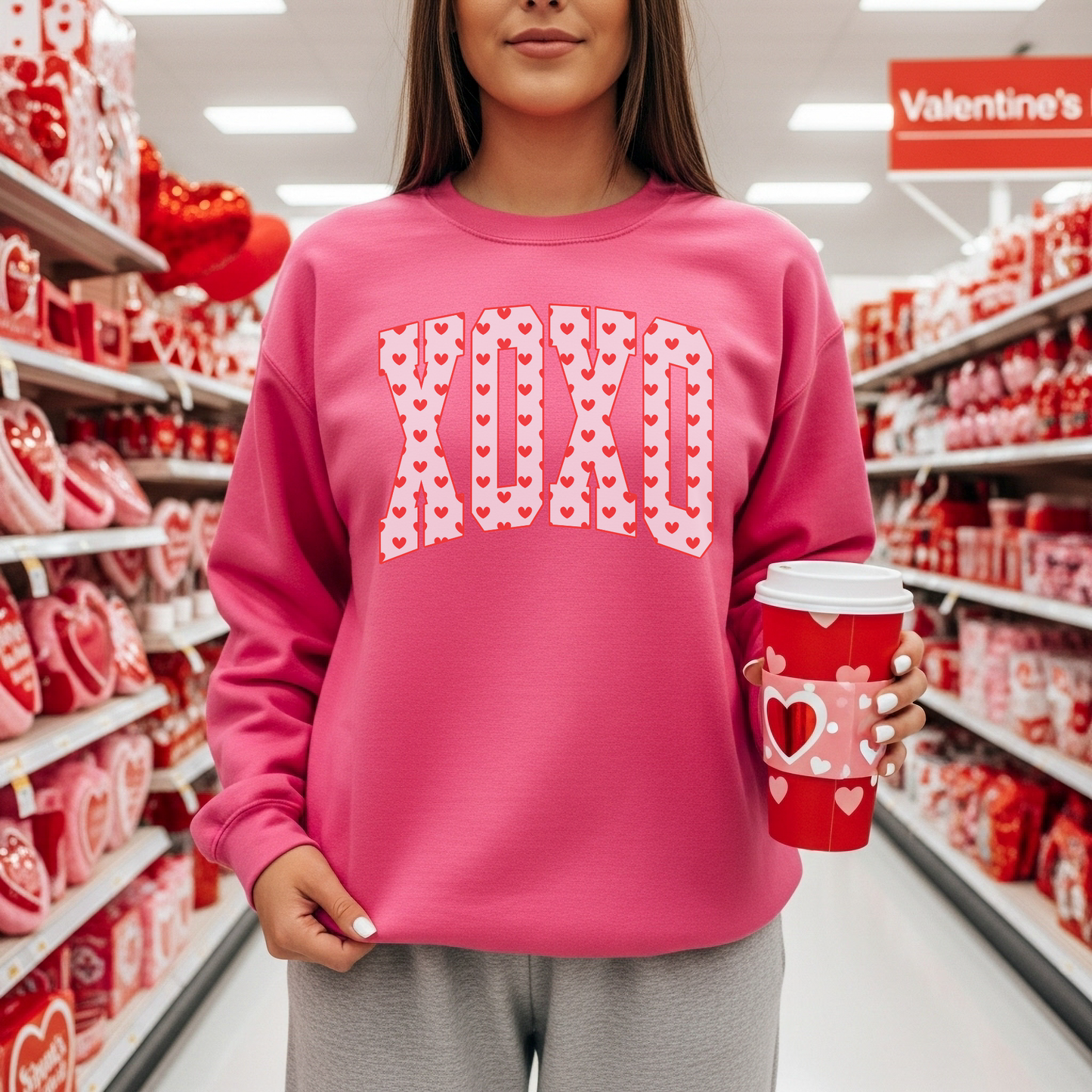 Model wearing pink XO Valentine sweatshirt shopping in Valentine’s Day store aisle holding coffee cup
