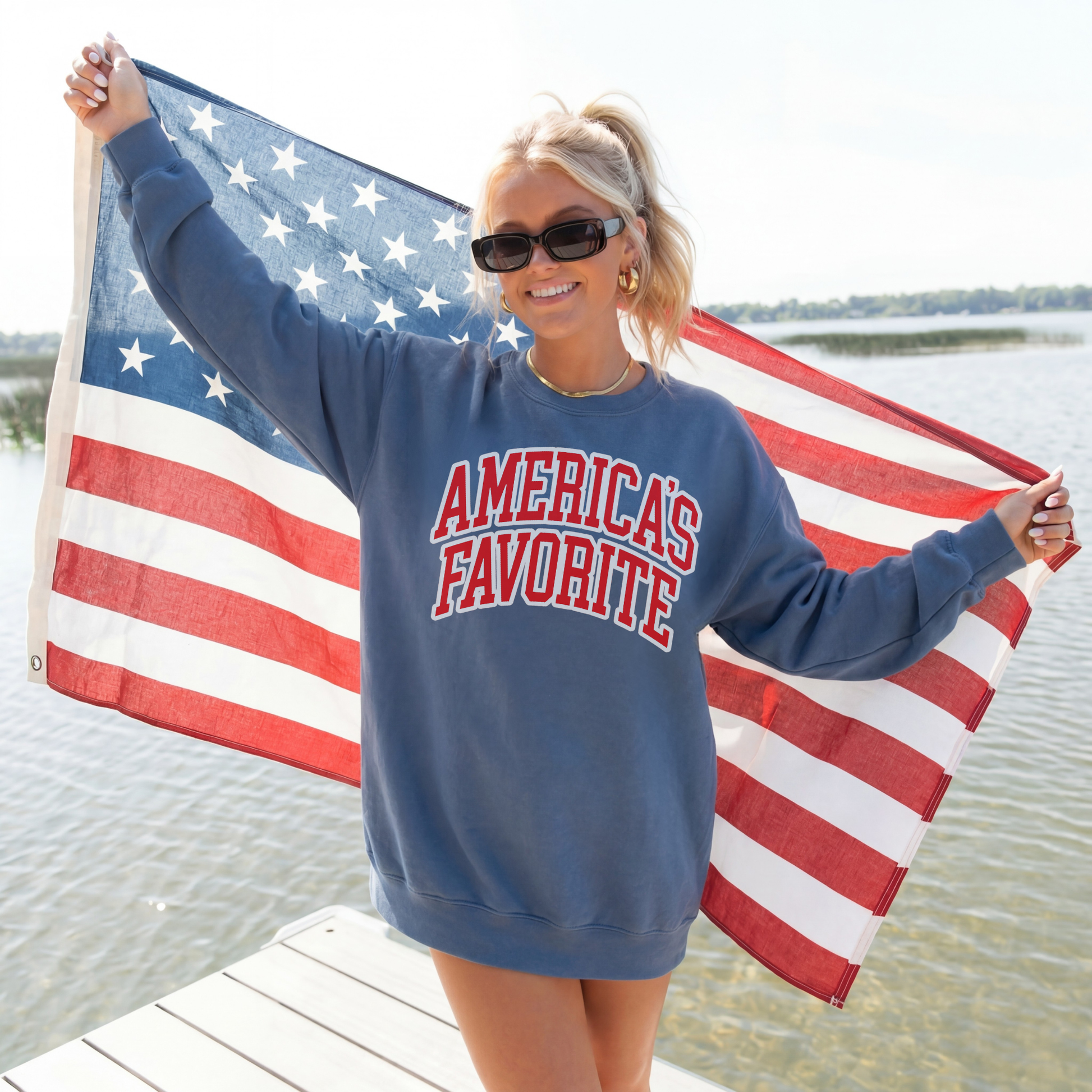Woman wearing oversized indigo blue America’s Favorite crewneck sweatshirt with American flag by the water.