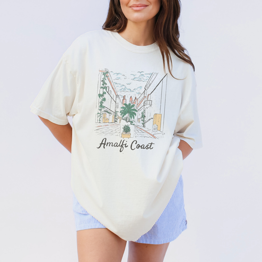 Woman wearing ivory Amalfi Coast graphic t-shirt with vintage Italy street illustration on the front.