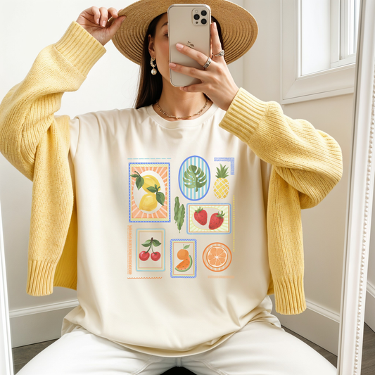 Model wearing a size Large ivory fruit block graphic tee, yellow cardigan, and straw hat while taking a mirror selfie.