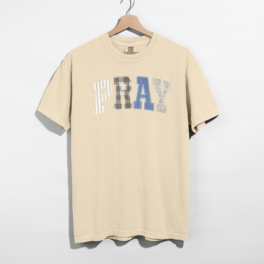 Beige t-shirt with 'PRAY' text on a hanger against a white background