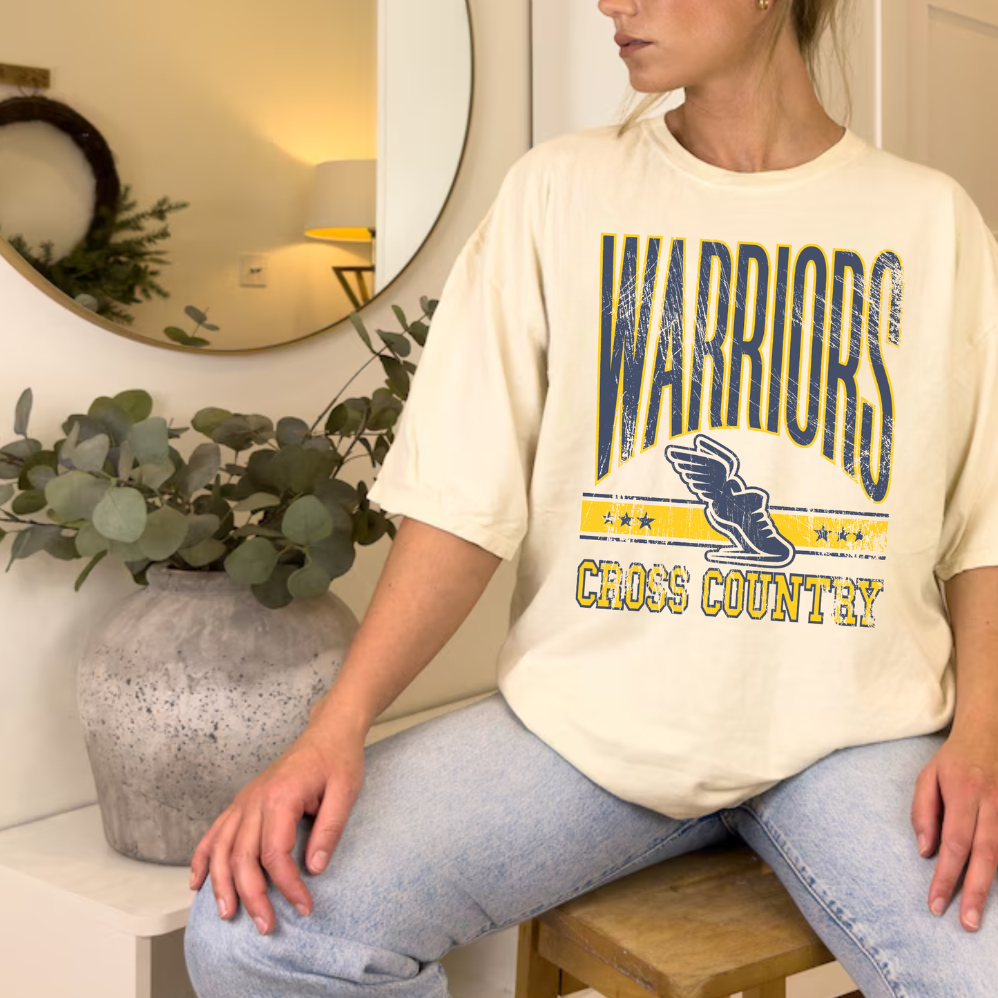 Ivory Warriors Cross Country school spirit shirt styled casually with jeans and neutral decor background