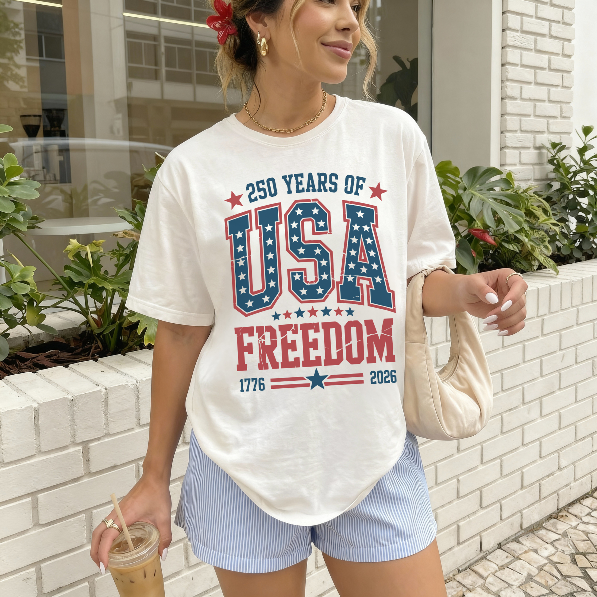 Woman wearing 250 Years of USA Freedom patriotic graphic tee styled with striped shorts and summer accessories