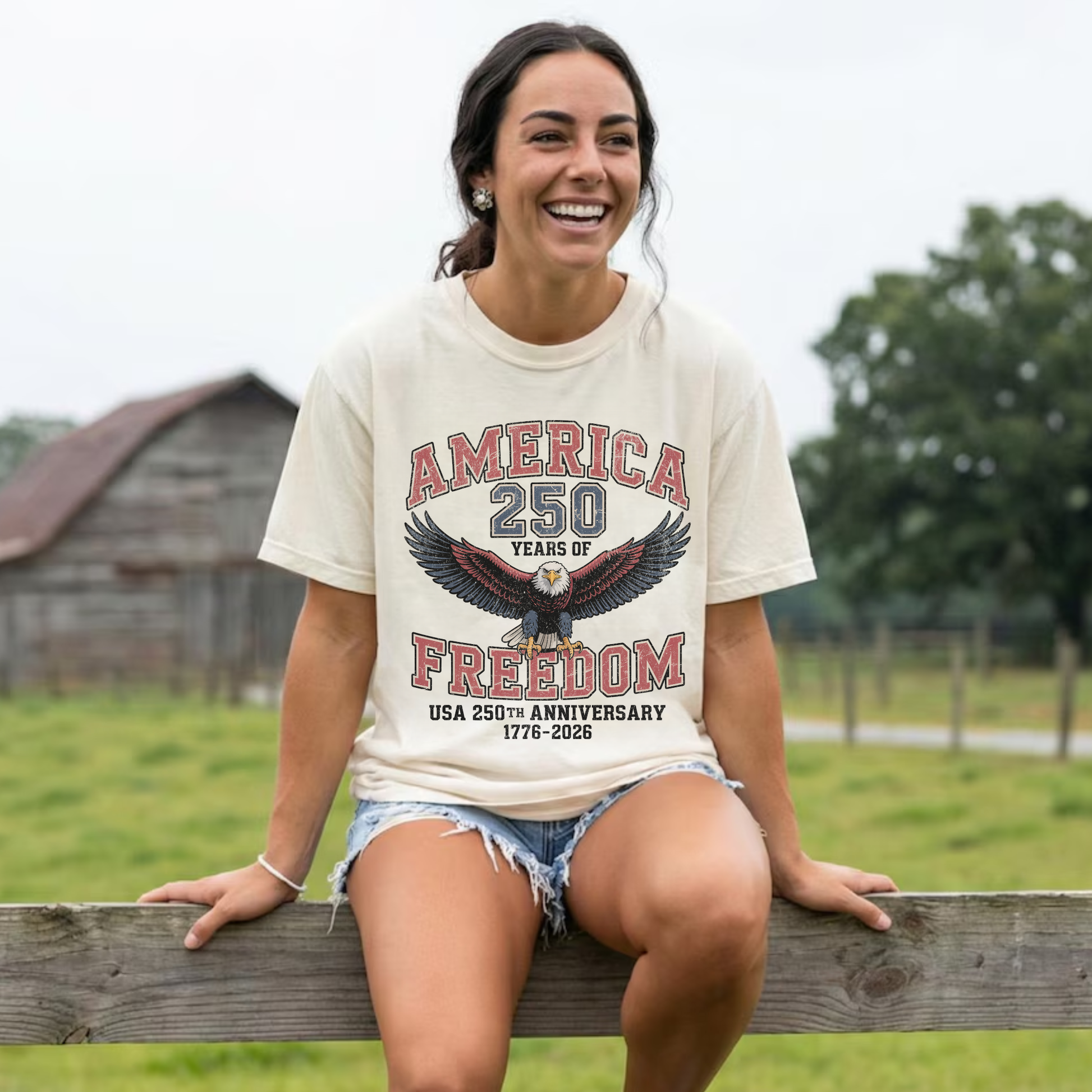 Woman wearing ivory America 250 Years of Freedom patriotic graphic t-shirt styled with denim shorts outdoors for summer Americana look.