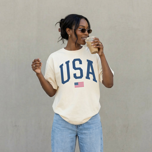 Woman wearing ivory USA varsity graphic tee drinking iced coffee minimal patriotic outfit