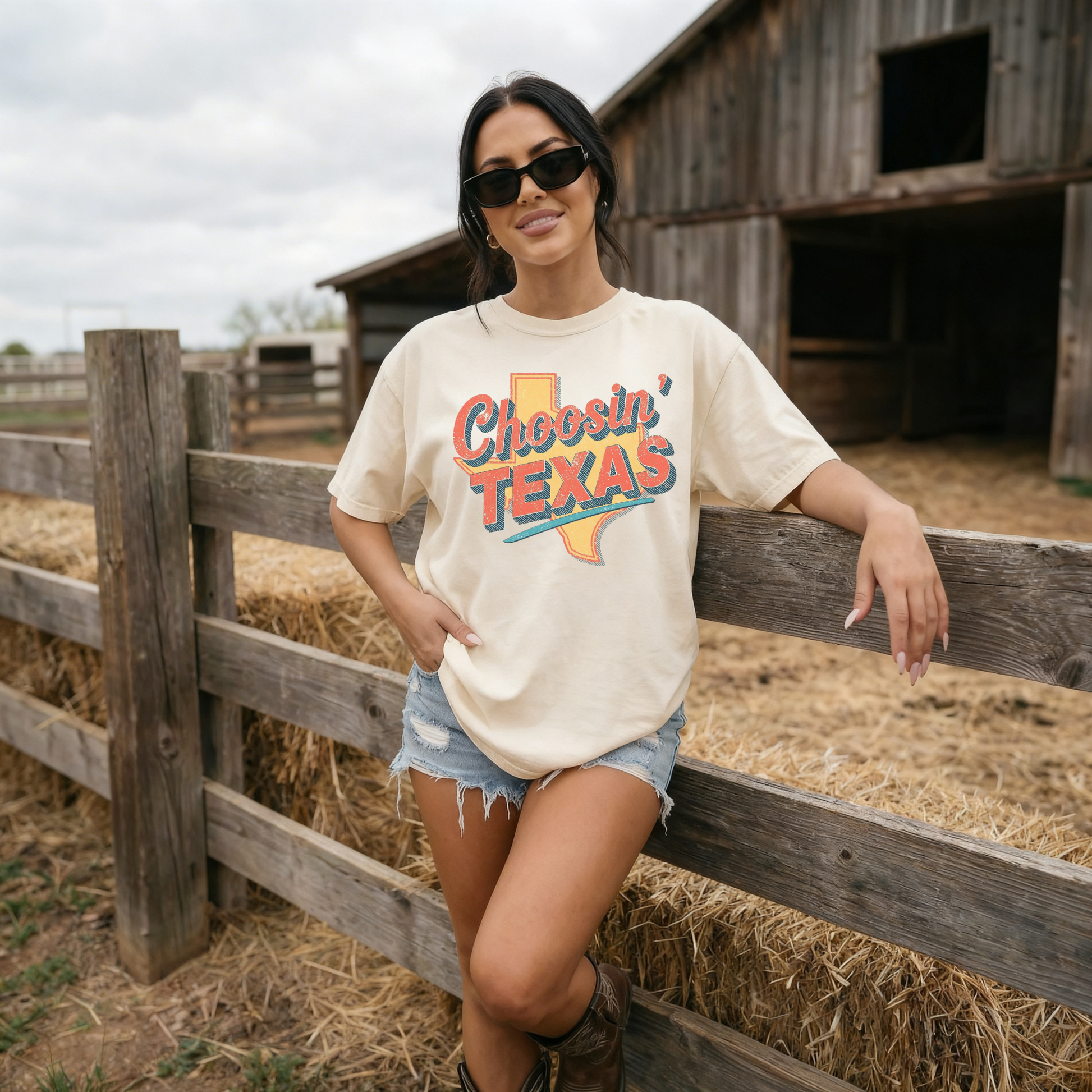 Woman wearing ivory Choosin Texas retro western graphic tee with denim shorts and boots at rustic barn
