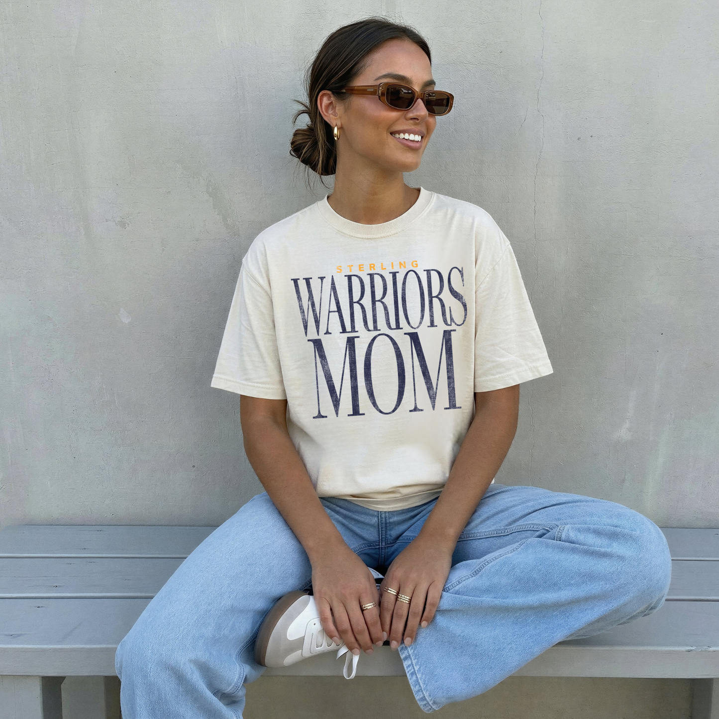 Sterling Warriors Mom ivory t-shirt worn by woman sitting on bench with light denim jeans neutral aesthetic casual outfit