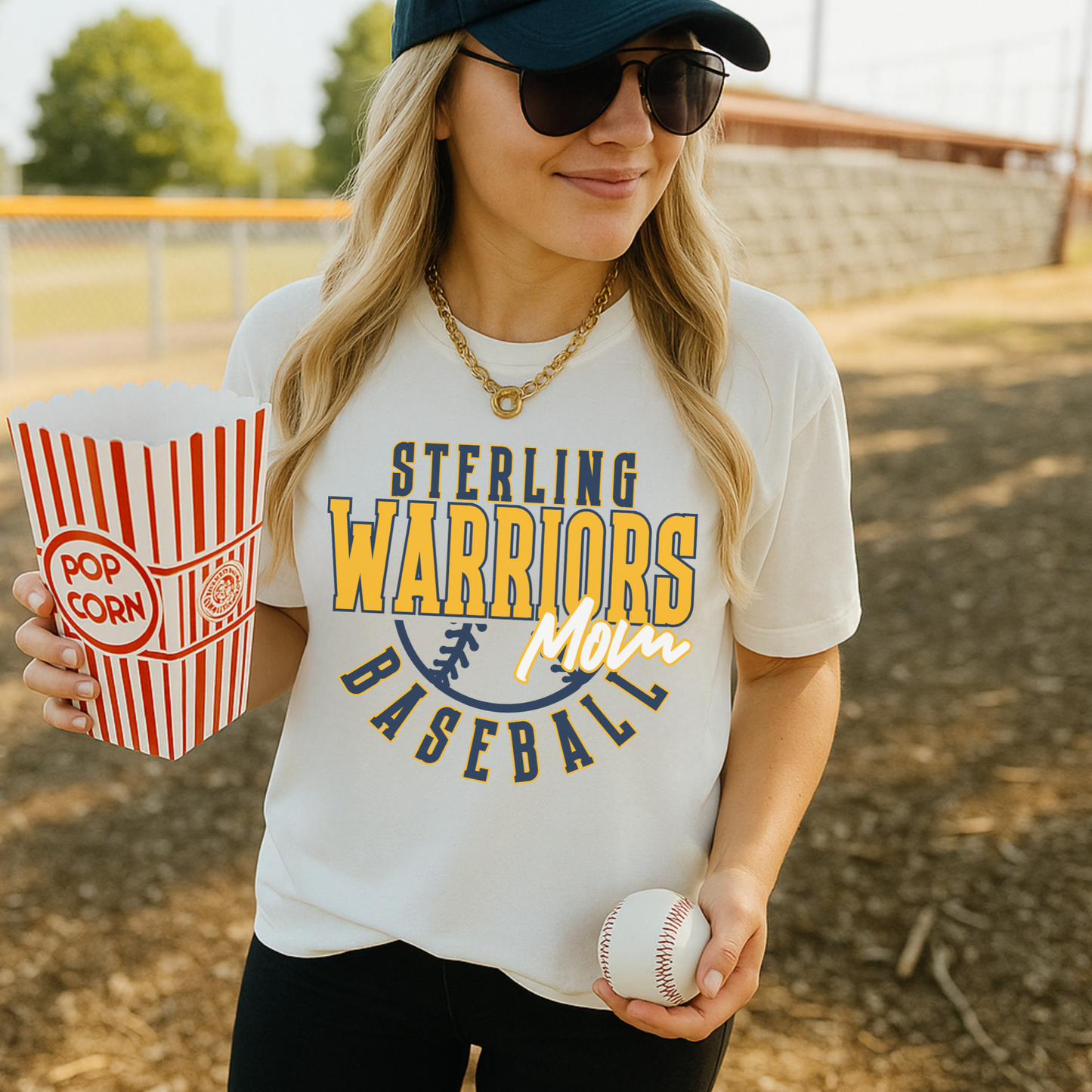 Sterling Warriors Baseball Mom t-shirt worn by woman holding popcorn and baseball at outdoor field casual game day outfit