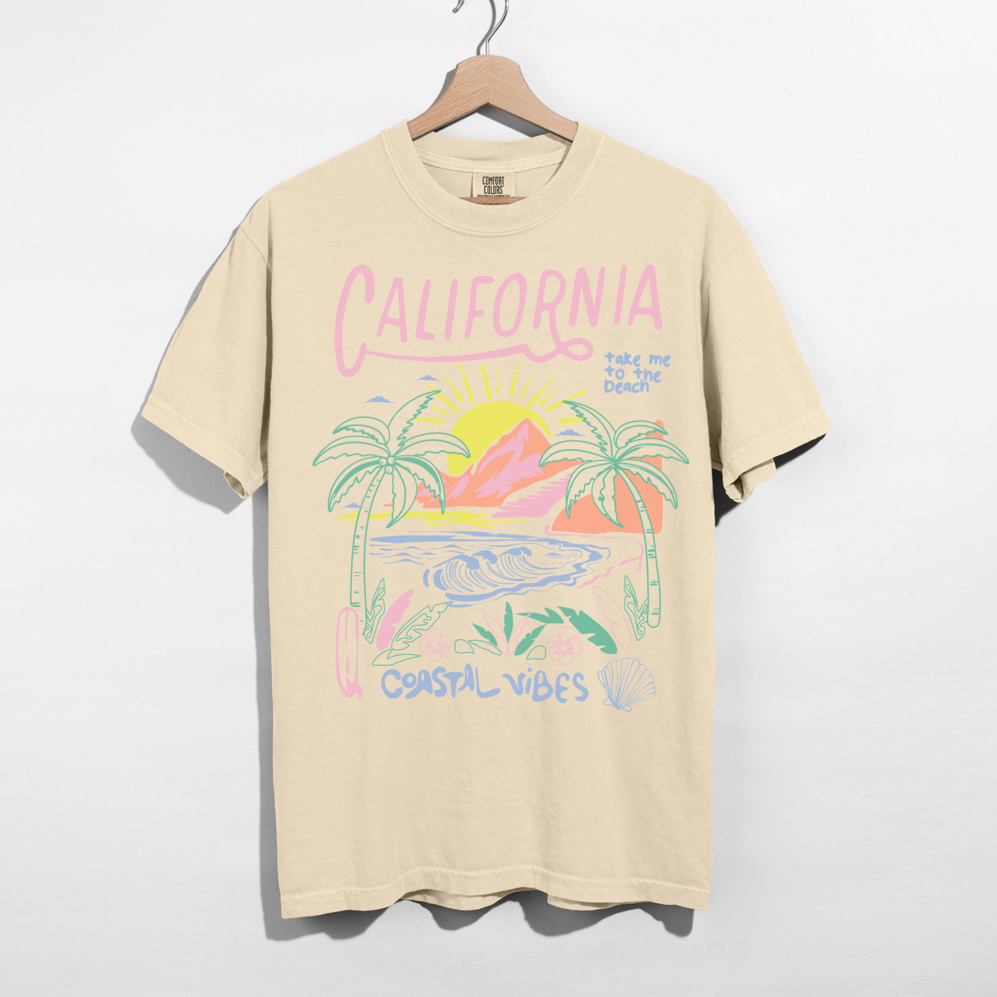 Ivory California Coastal Vibes tee with palm tree sunset design on hanger