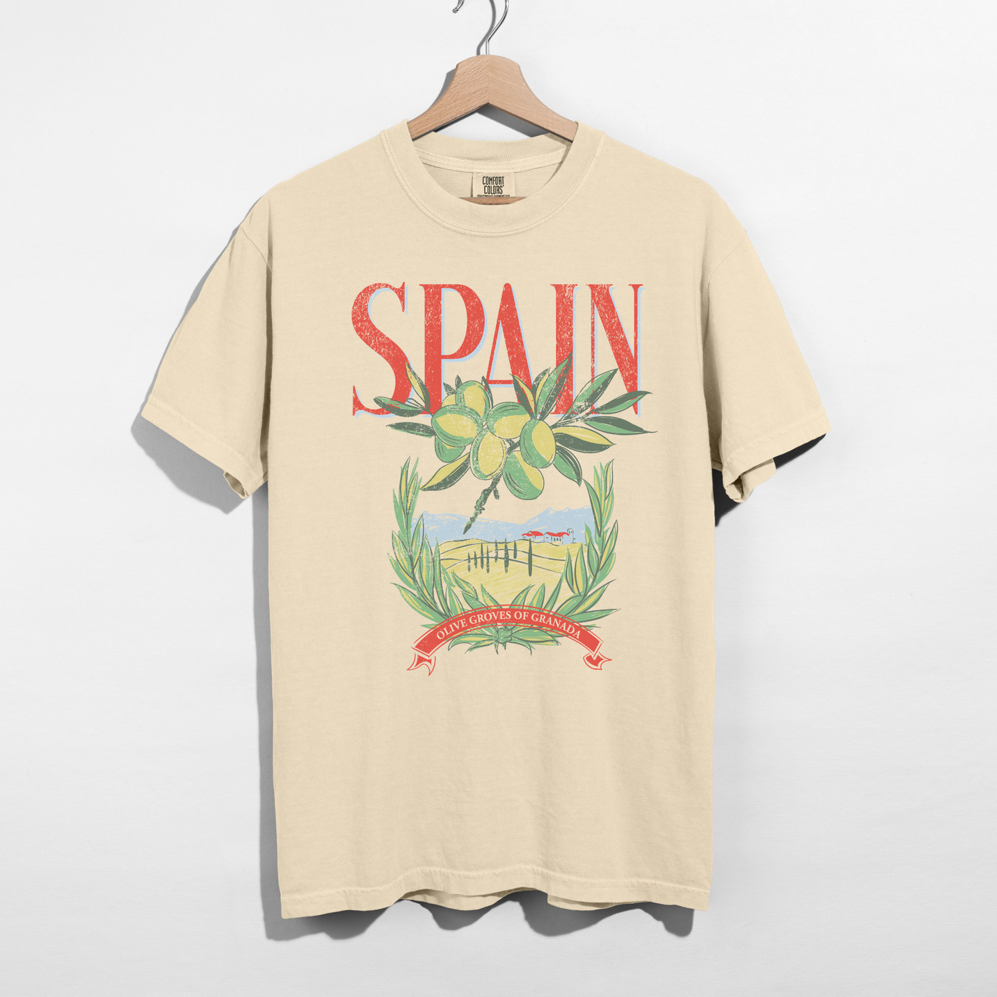 Ivory Comfort Colors Spain graphic tee with olive branches and countryside illustration on hanger