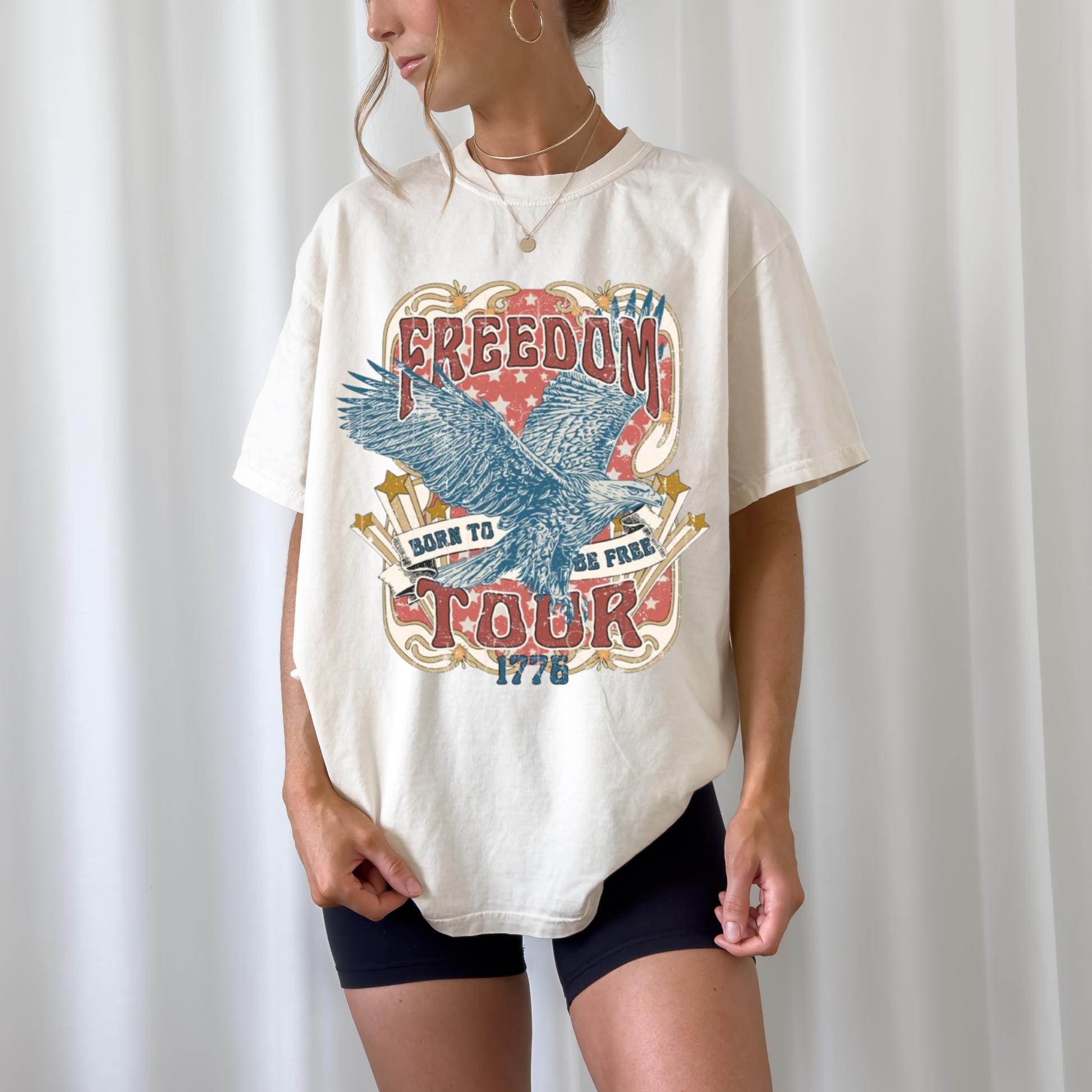 A person wearing a ivory graphic tee with 'Freedom Tour 1776' text and an eagle design.
