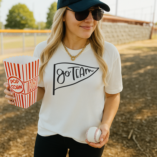 Woman at a baseball game holding popcorn and a ball, wearing a 'Go Team' shirt.