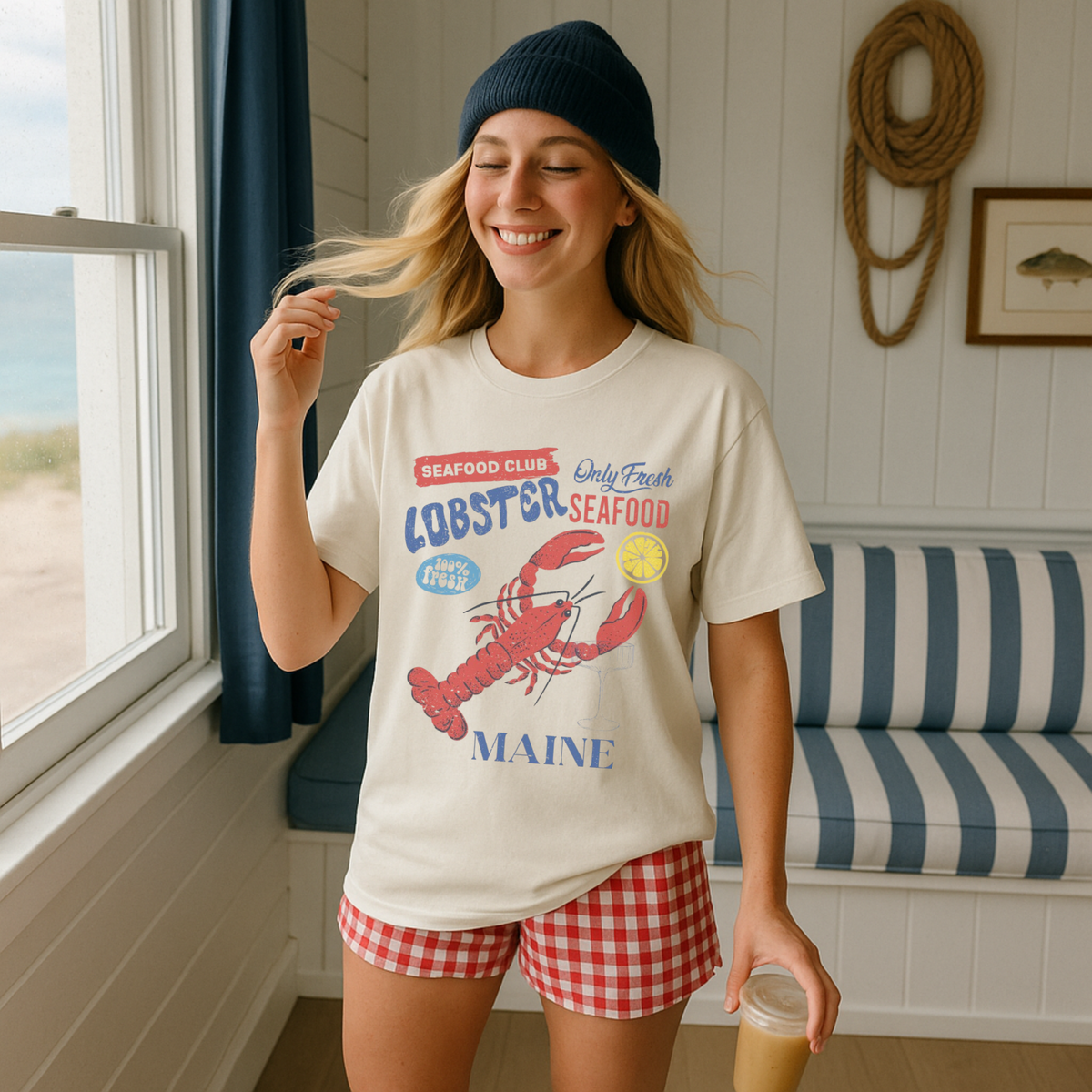 Woman wearing a t-shirt with a lobster graphic and 'Maine' text in a coastal room.