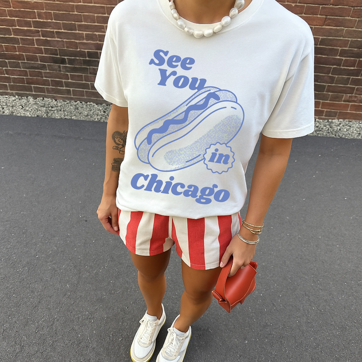 Woman wearing ivory Chicago hot dog graphic tee styled with red striped shorts and sneakers