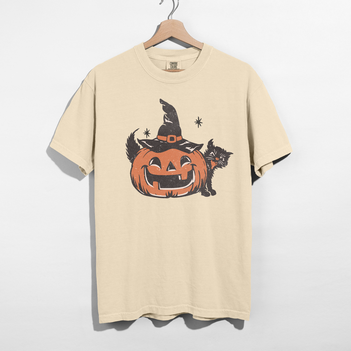 Ivory Halloween graphic t-shirt on wooden hanger featuring a retro orange jack-o'-lantern with black witch hat, black cat, and distressed vintage print.
