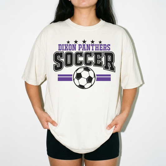 A person wearing an oversized cream-colored t-shirt with a 'Dixon Panthers Soccer' graphic in purple and black, paired with black shorts, against a plain white background.