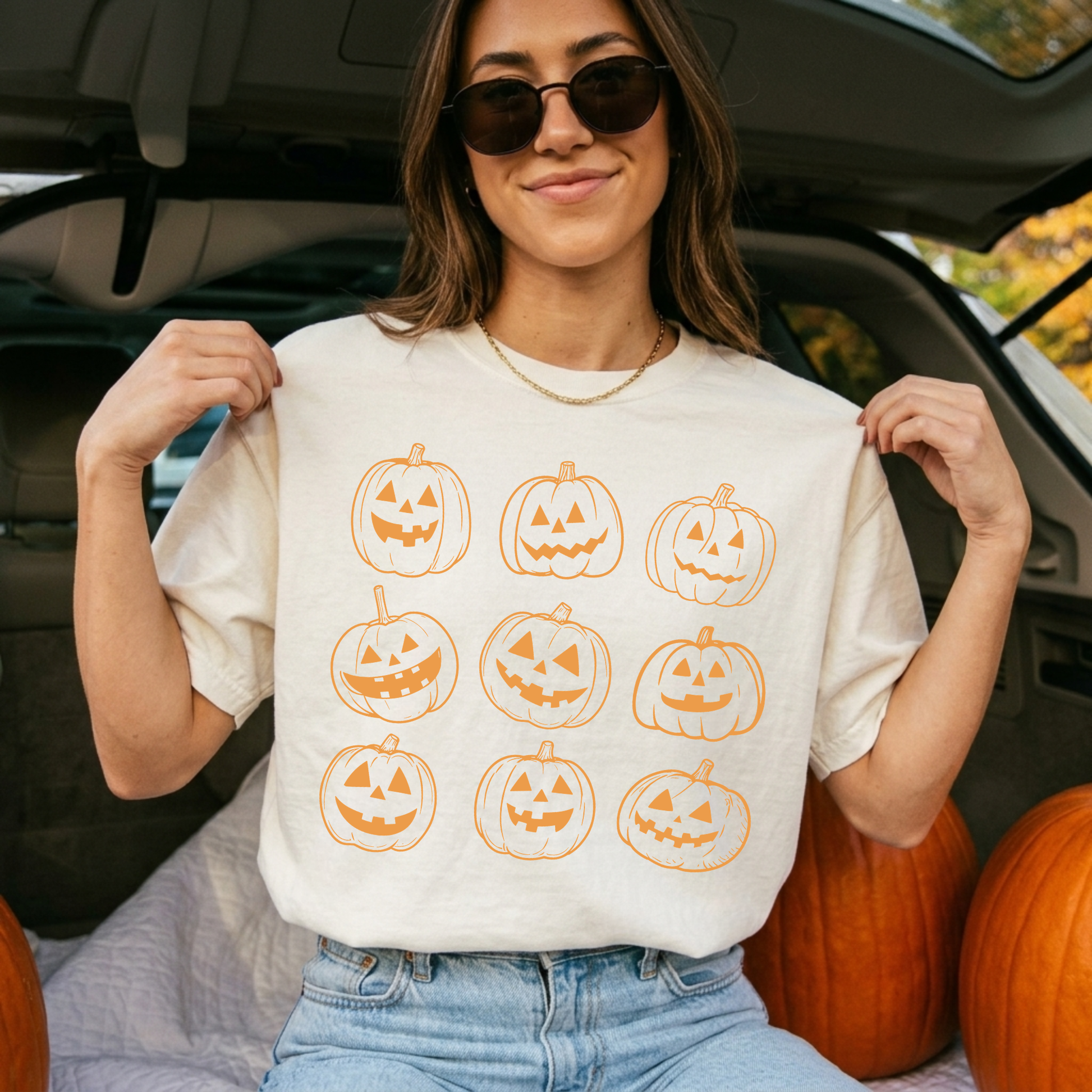 Woman wearing an ivory Comfort Colors pumpkin graphic tee with vintage orange jack o' lantern artwork while sitting at the back of an SUV decorated for fall.