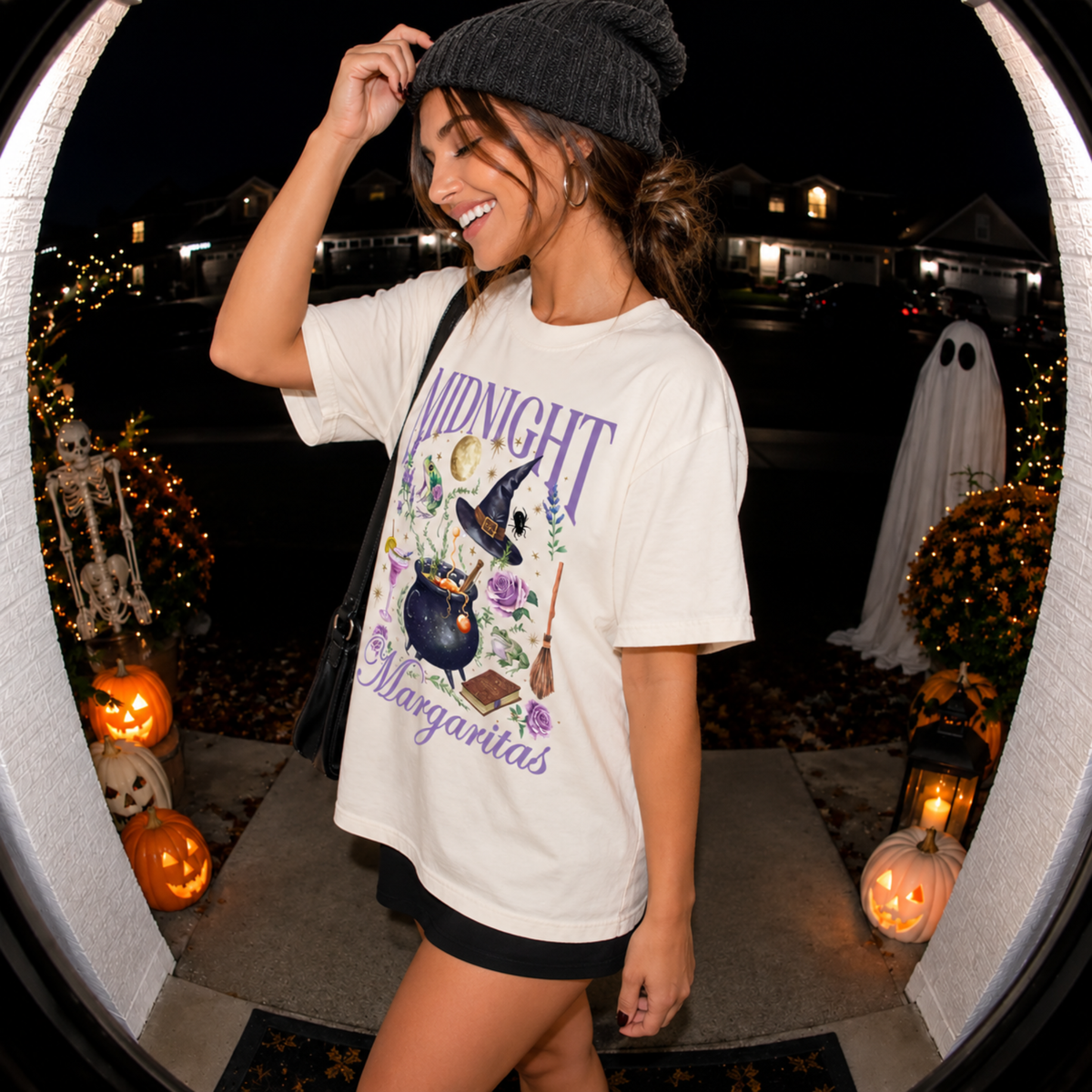 Side view of woman styling an ivory Midnight Margaritas Halloween t-shirt with black skirt, shoulder bag, and knit beanie surrounded by glowing jack-o'-lanterns.