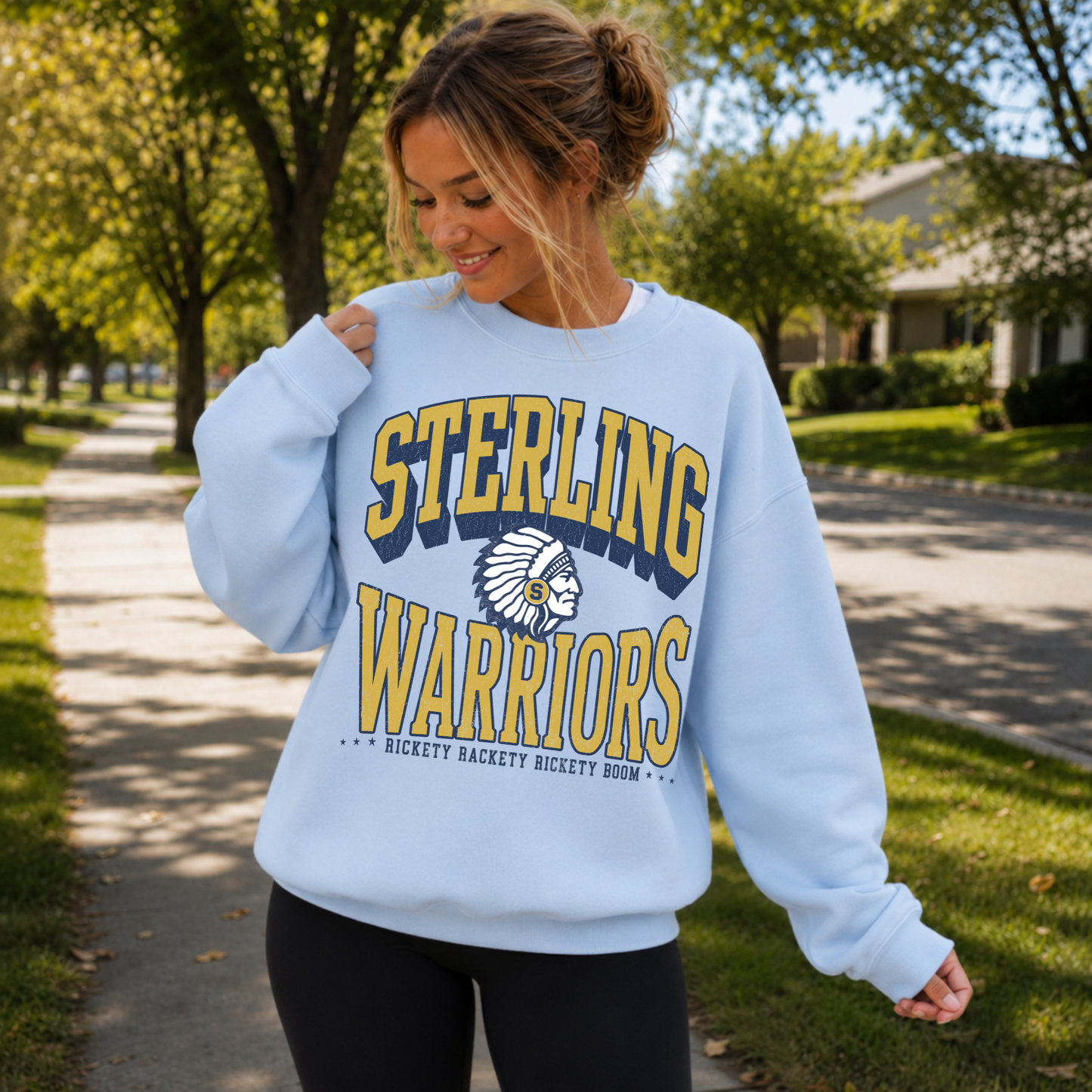 Woman modeling a light blue Sterling Warriors sweatshirt with vintage Warrior mascot graphic and Rickety Rackety Rickety Boom slogan.
