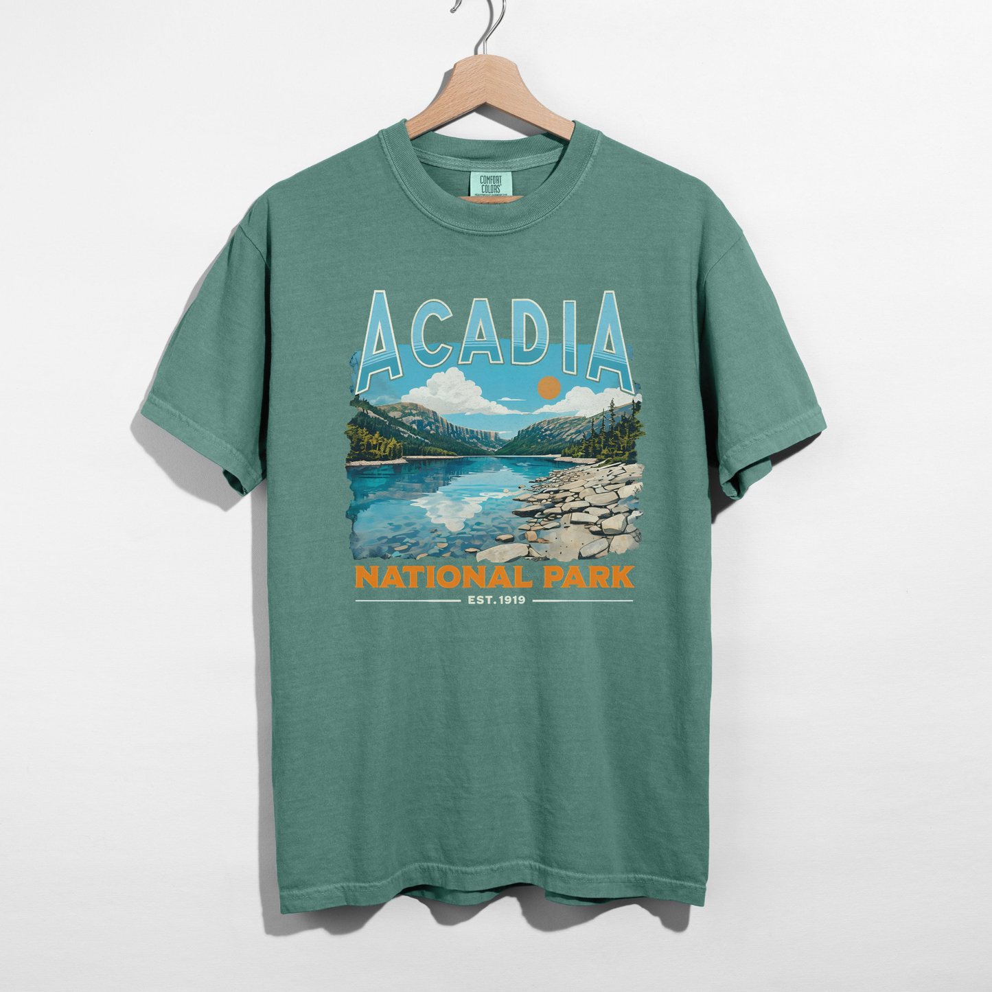 green Acadia National Park vintage graphic t-shirt hanging on wooden hanger with colorful scenic national park print.