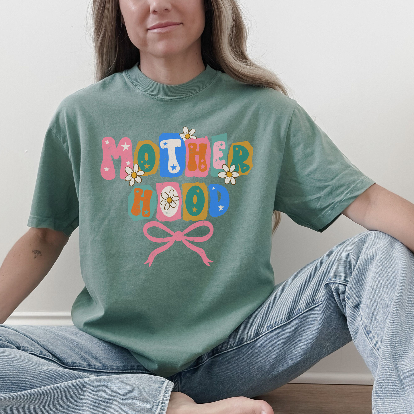 “Woman wearing light green Motherhood retro floral bow graphic tee.”