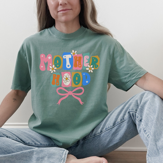 “Woman wearing light green Motherhood retro floral bow graphic tee.”