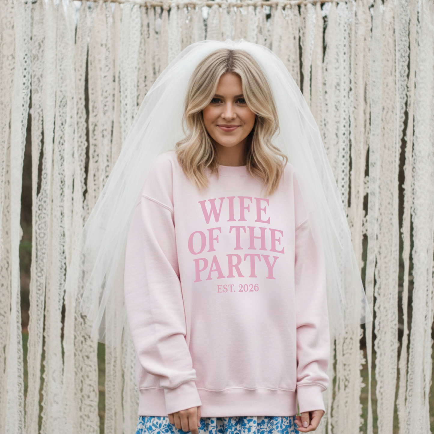 Bride wearing white “Wife of the Party Est. 2026” crewneck sweatshirt at bridal celebration with pastel balloon decor