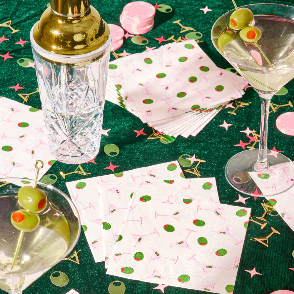 Cocktail glasses with garnishes on a tablecloth with cocktail-themed decorations.