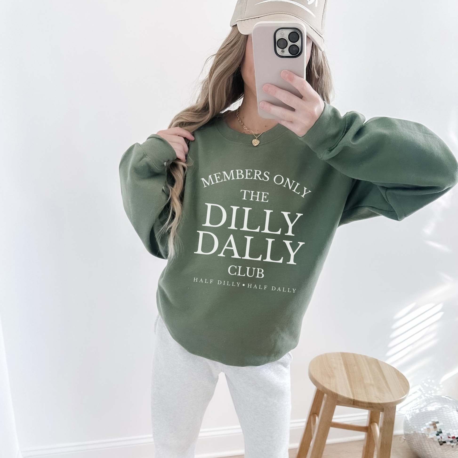Woman wearing a military green “Dilly Dally Club” crewneck sweatshirt taking a mirror selfie.