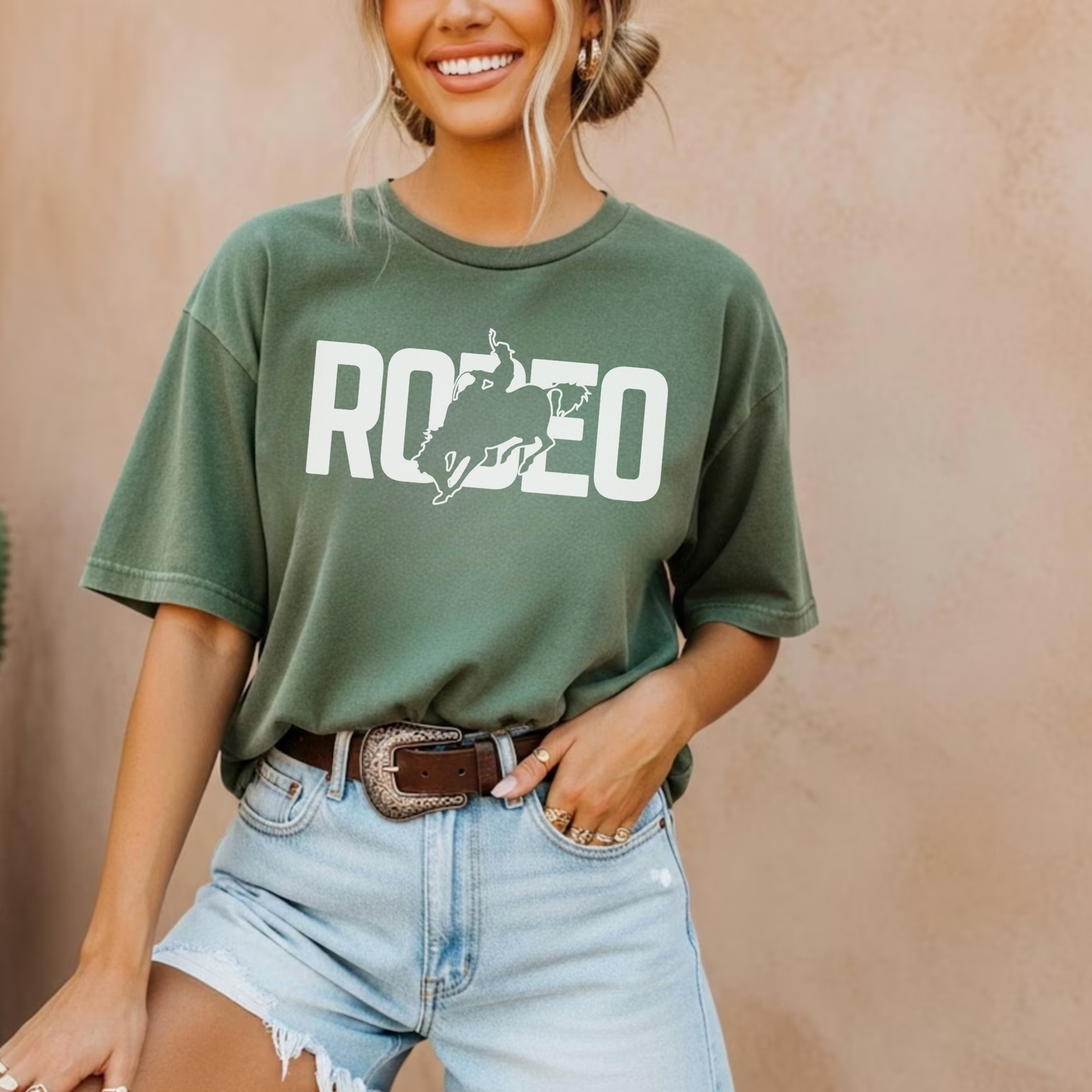Woman wearing green western rodeo graphic tee with denim shorts and belt outdoors