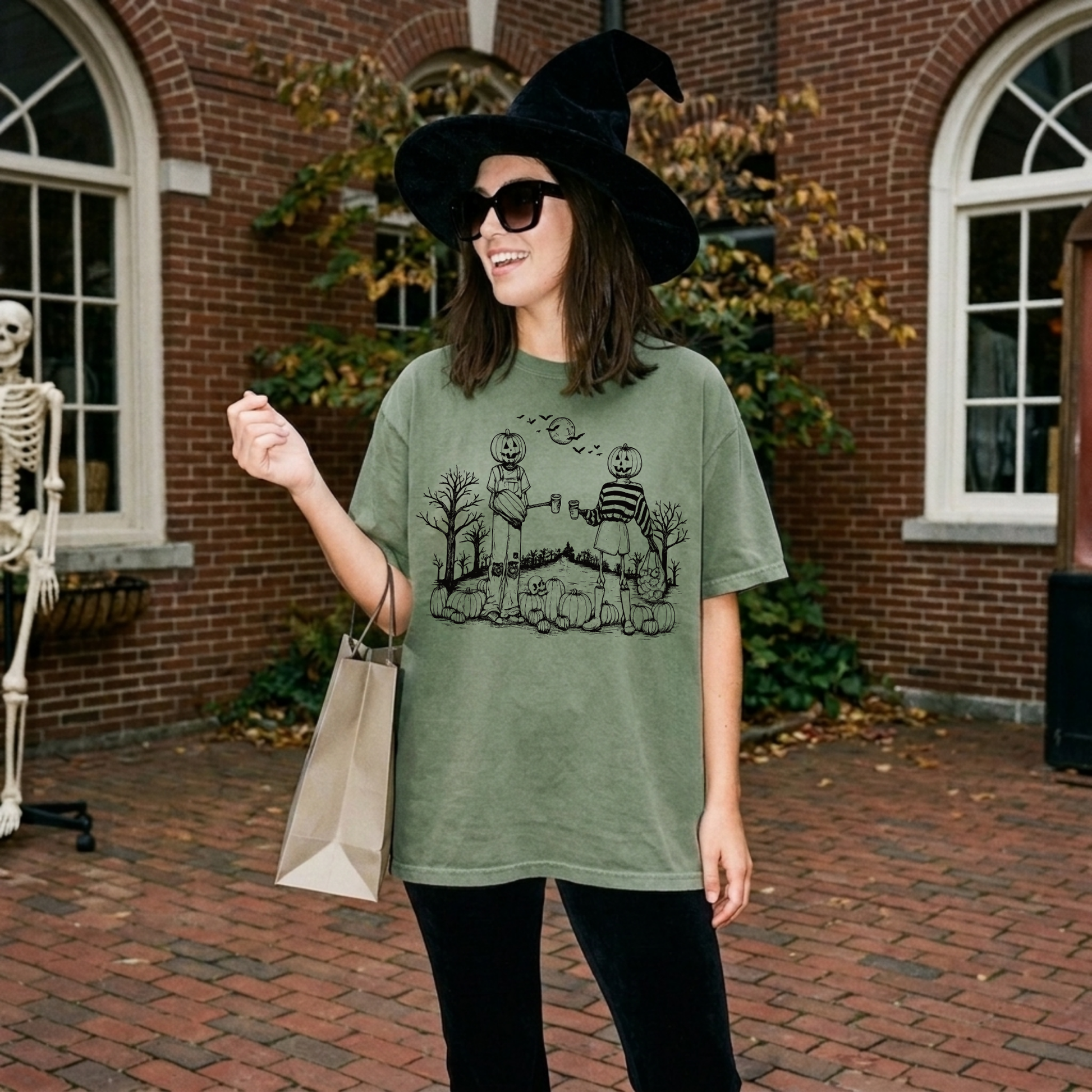 Woman wearing a moss green Halloween pumpkin patch graphic tee with pumpkin-headed friends and spooky fall artwork outside in autumn.