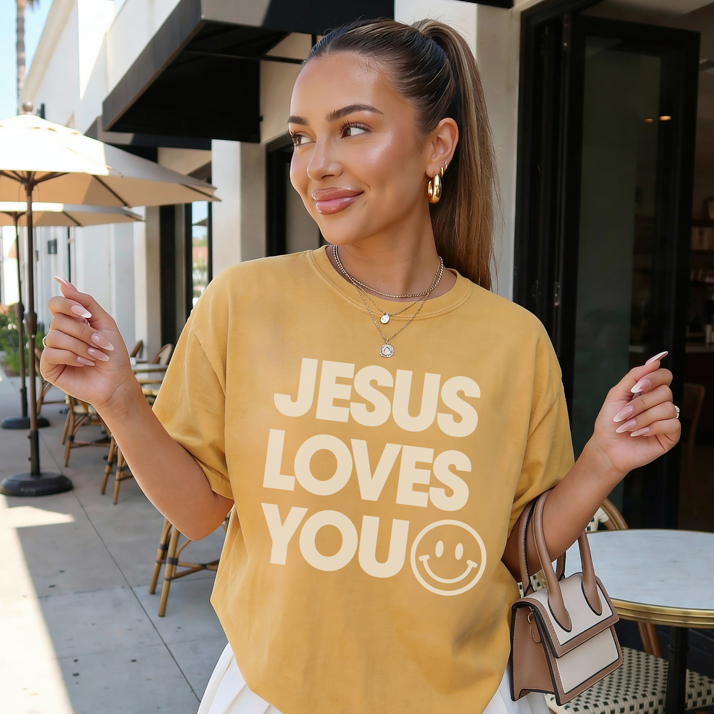 Jesus Loves You graphic t shirt in mustard worn casually outdoors featuring inspirational Christian message