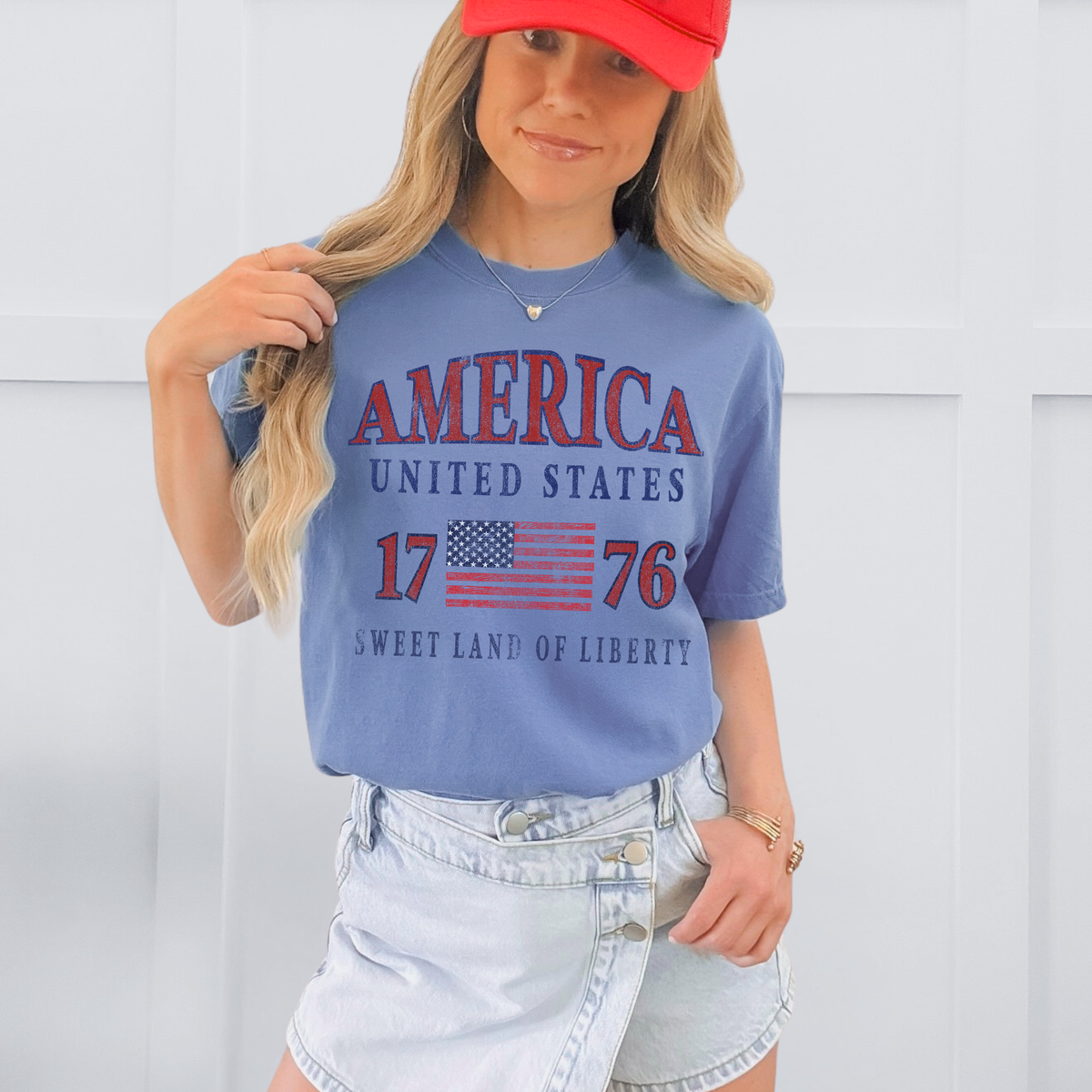 Person wearing a blue t-shirt with 'America United States 1776 Sweet Land of Liberty' text and a red cap.