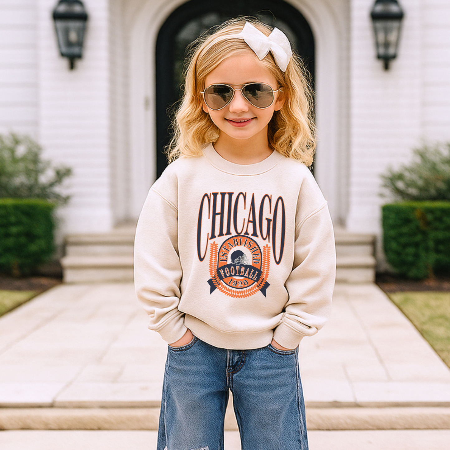 Child wearing a 'Chicago' sweatshirt and sunglasses in front of a house.
