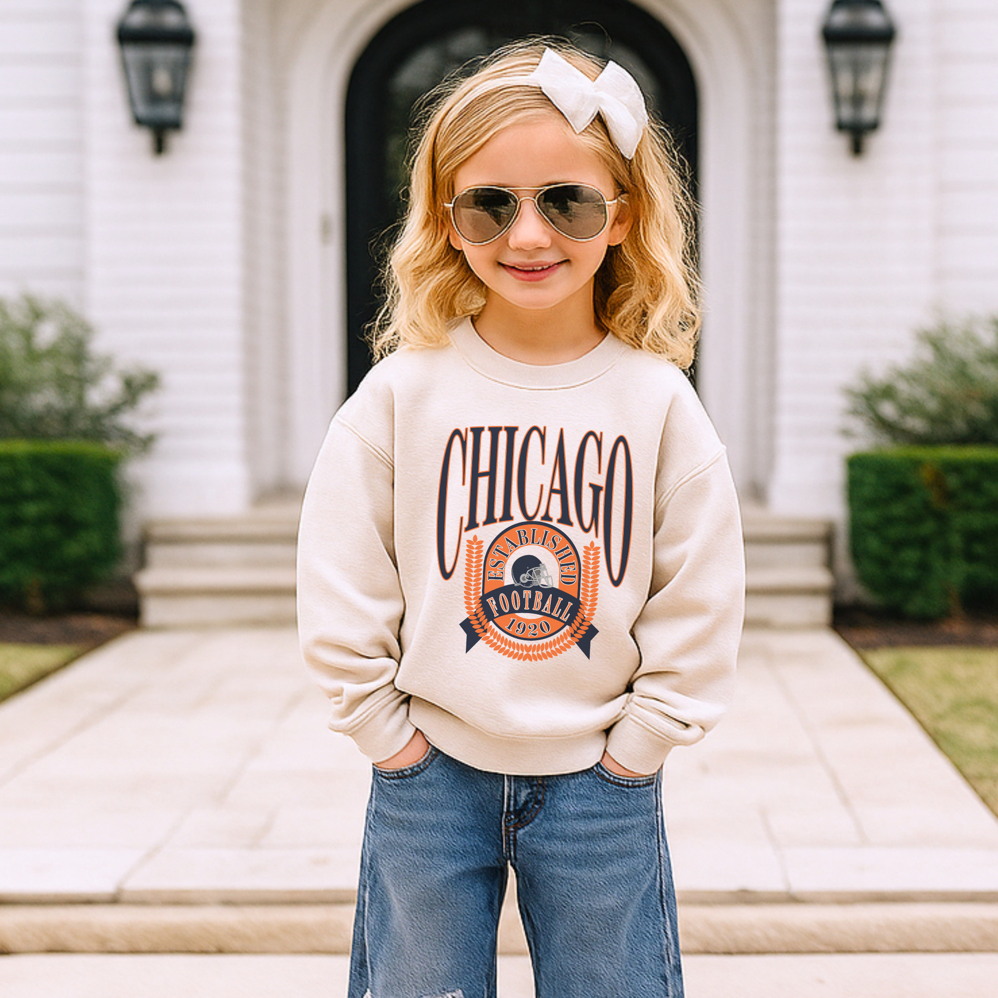 Child wearing a 'Chicago' sweatshirt and sunglasses in front of a house.