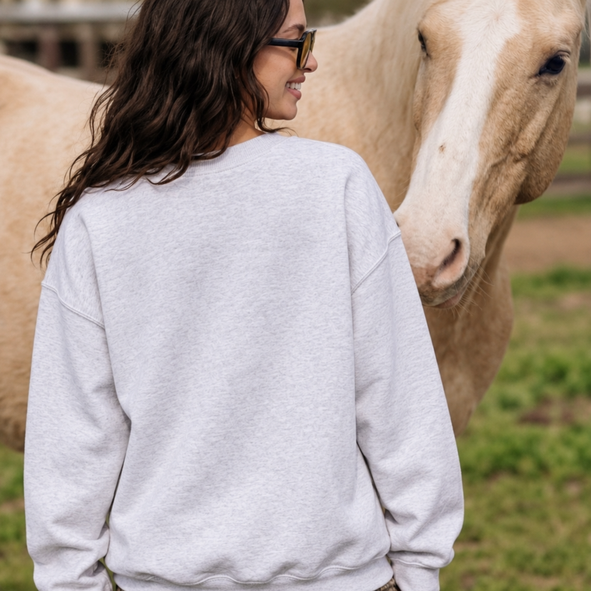 Back view of woman wearing a heather grey crewneck sweatshirt while standing beside a horse