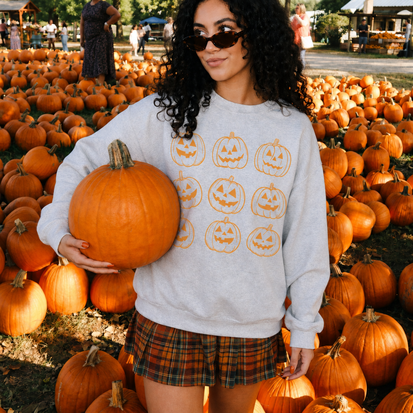 Woman wearing vintage pumpkin Halloween sweatshirt while holding pumpkin at pumpkin patch
