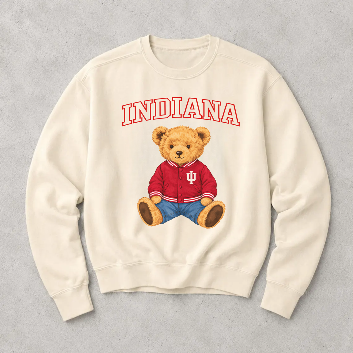 Off white Indiana collegiate teddy bear sweatshirt with red outlined Indiana lettering and an adorable golden teddy bear wearing a crimson varsity jacket and blue jeans.