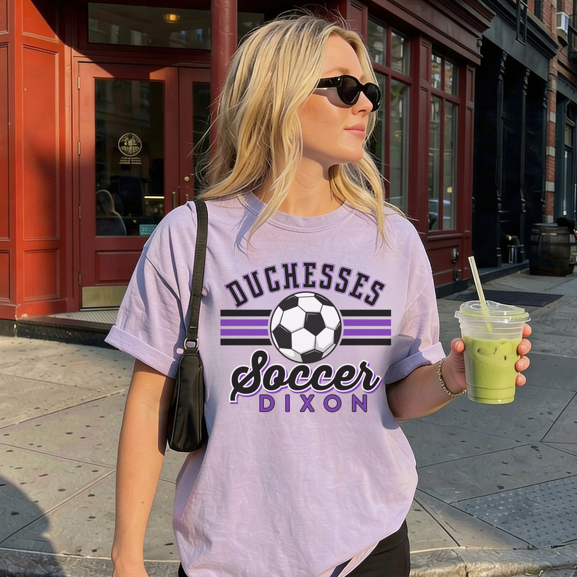 Model wearing purple Duchesses Soccer Dixon graphic t-shirt with sunglasses holding iced drink