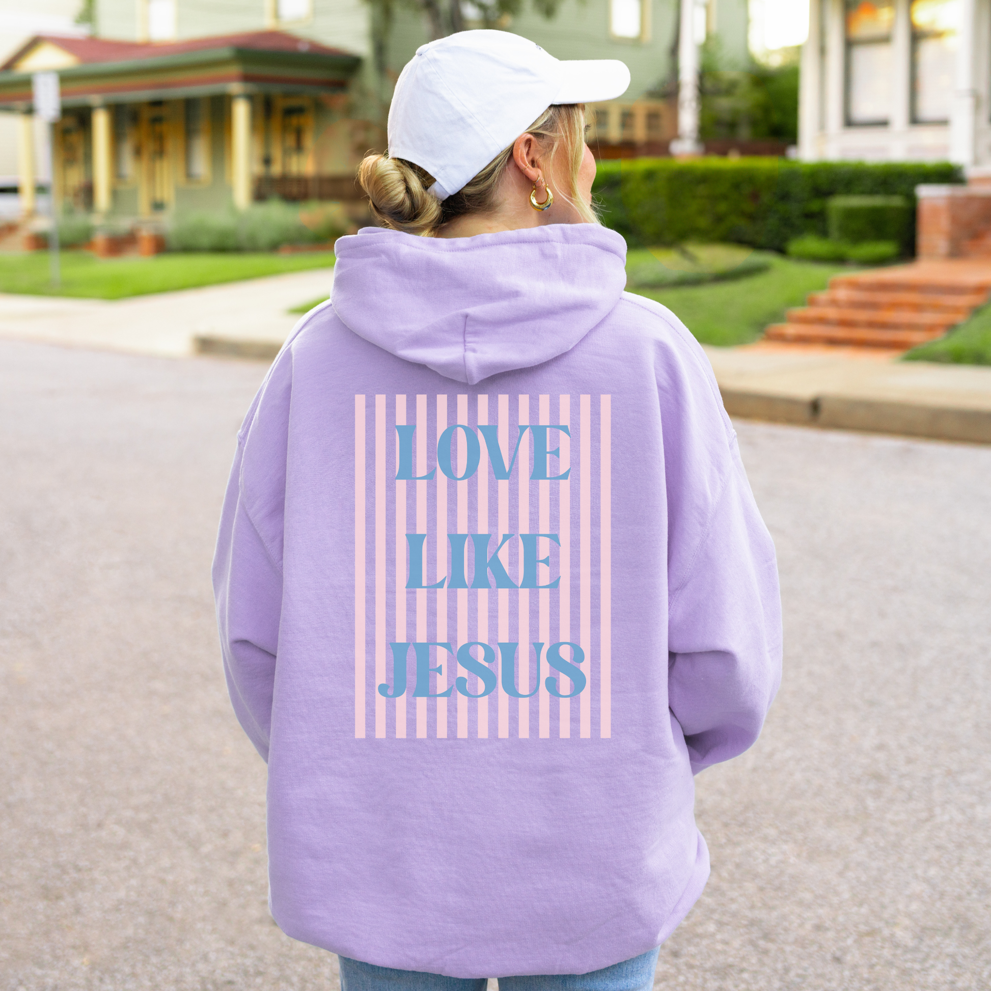 Woman wearing orchid pastel hoodie with large striped “Love Like Jesus” back graphic.