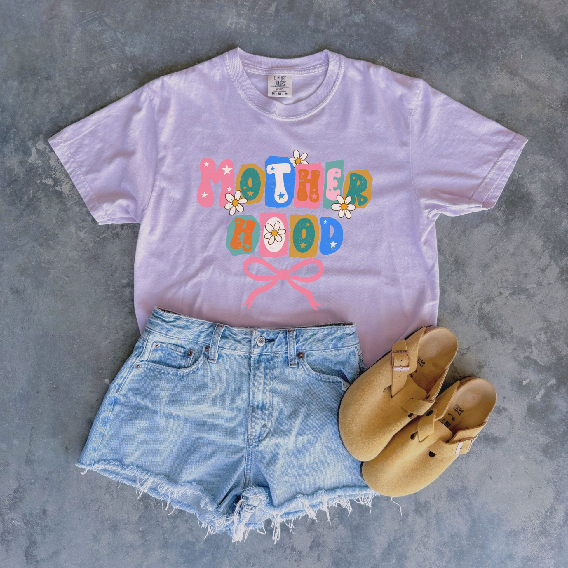 “Lavender Motherhood graphic tee styled with denim shorts and sandals.”