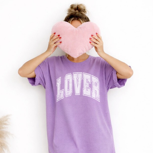 Model wearing lavender LOVER  graphic t-shirt holding pink heart pillow