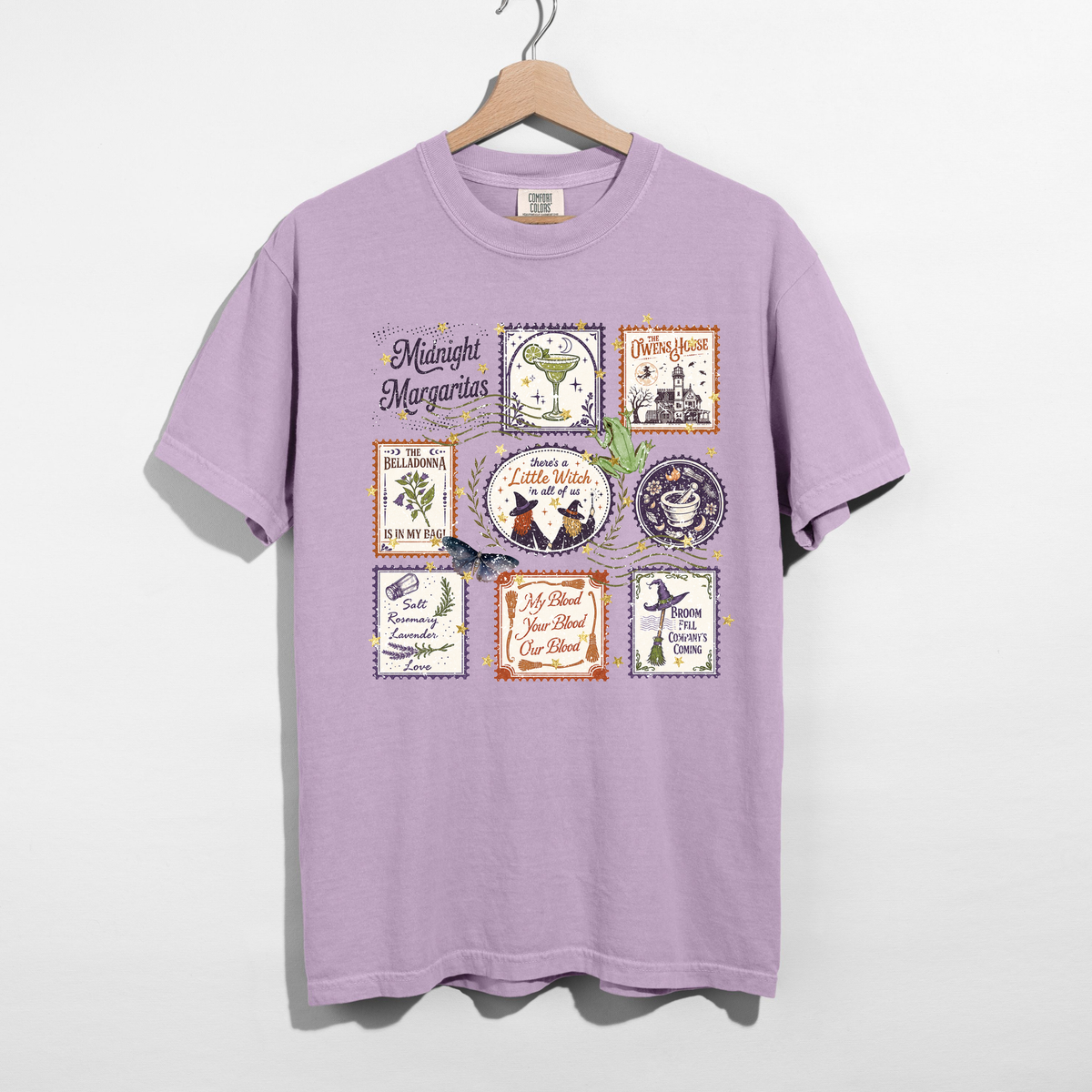 Orchid purple Midnight Margaritas Halloween graphic t-shirt hanging on wooden hanger, featuring vintage witchy postage stamps, margarita cocktail, botanical illustrations, and spooky sayings.