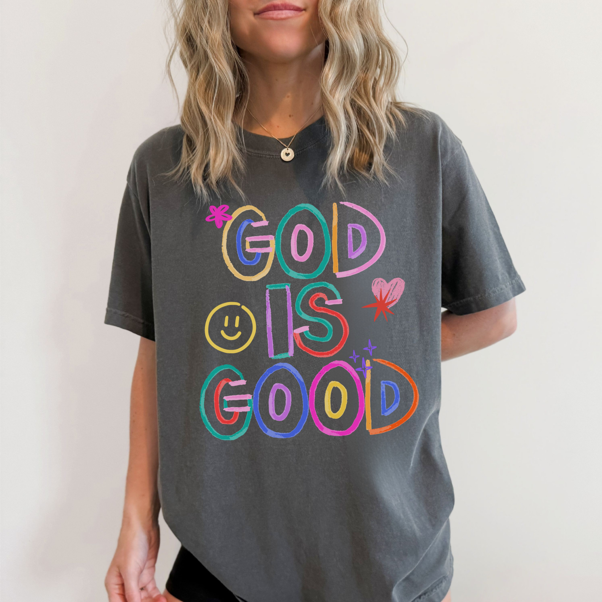 Person wearing a gray t-shirt with 'GOD IS GOOD' in colorful letters on a plain background