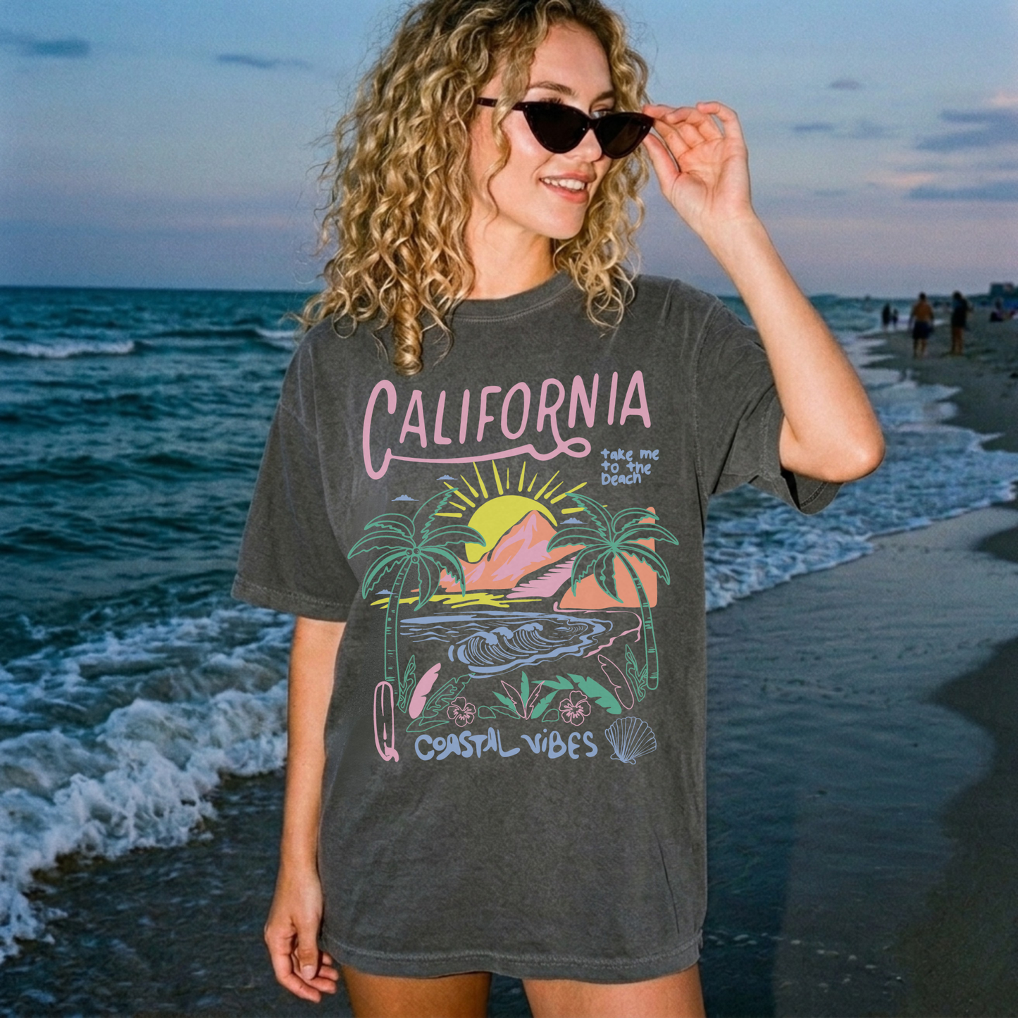 Model wearing pepper oversized California beach graphic tee walking along shoreline