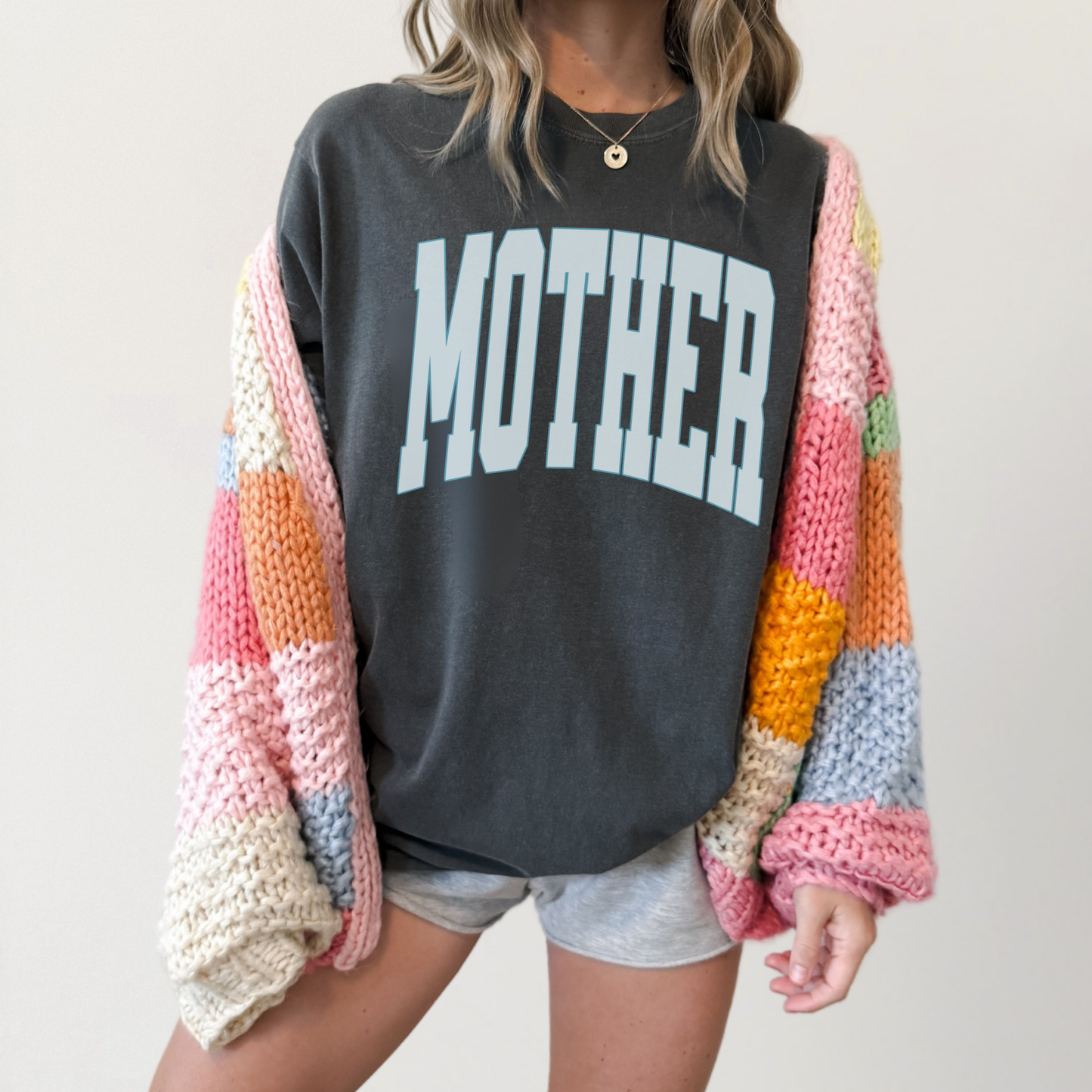 Charcoal gray graphic t-shirt with light blue “MOTHER” text layered under colorful knit cardigan