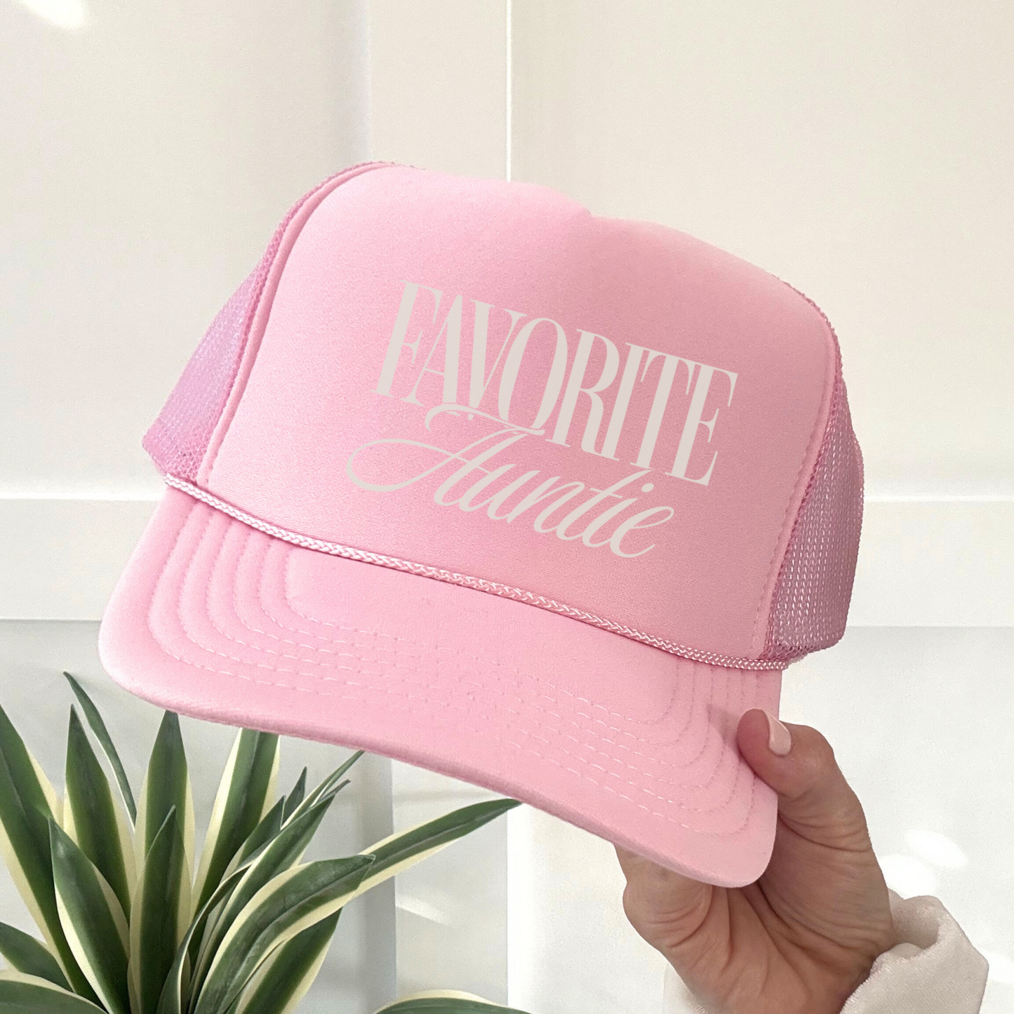 Pink cap with 'Favorite Auntie' text held by a hand against a light background